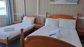 A hotel room with two wooden beds, white bedding, a painting on the wall, and a window with curtains.