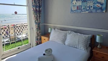 Une chambre d’hôtel avec un lit, un tableau représentant un paysage côtier, une fenêtre donnant sur la plage et un rideau.