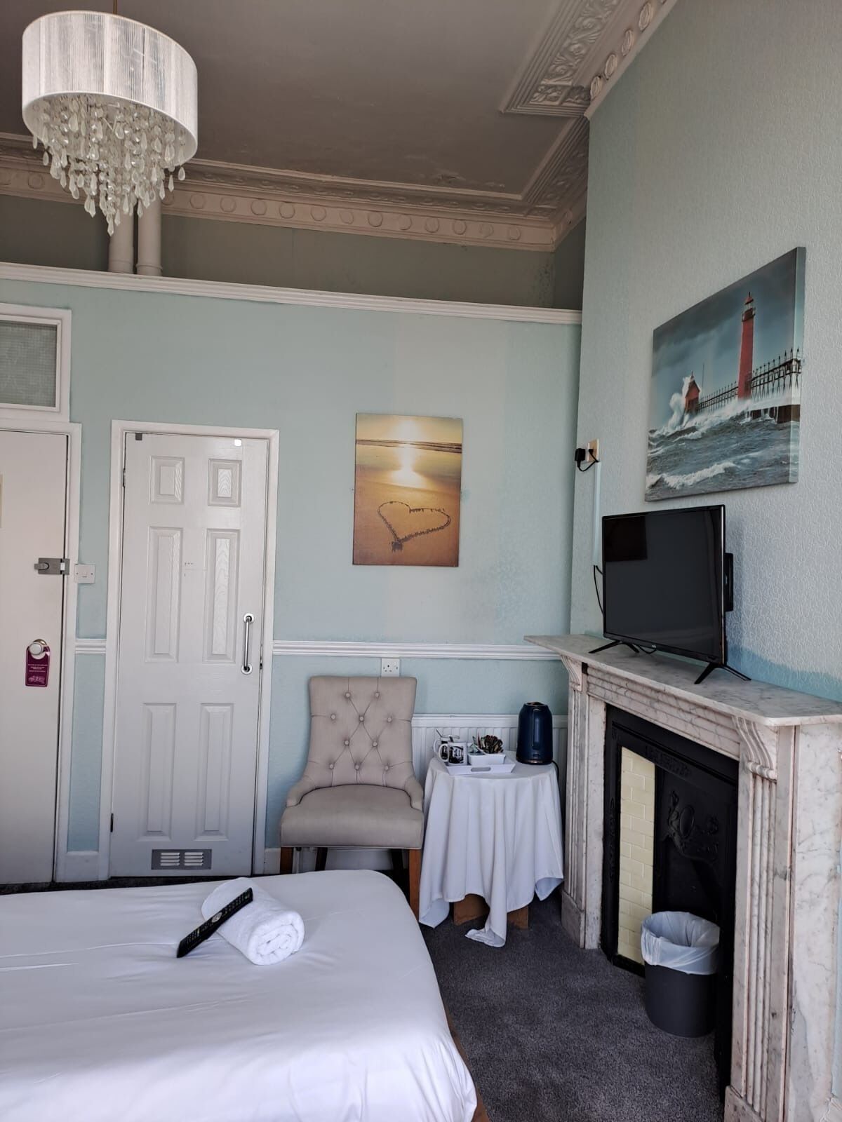 A hotel room with a bed, a chair, a television, a fireplace, and a painting on the wall.