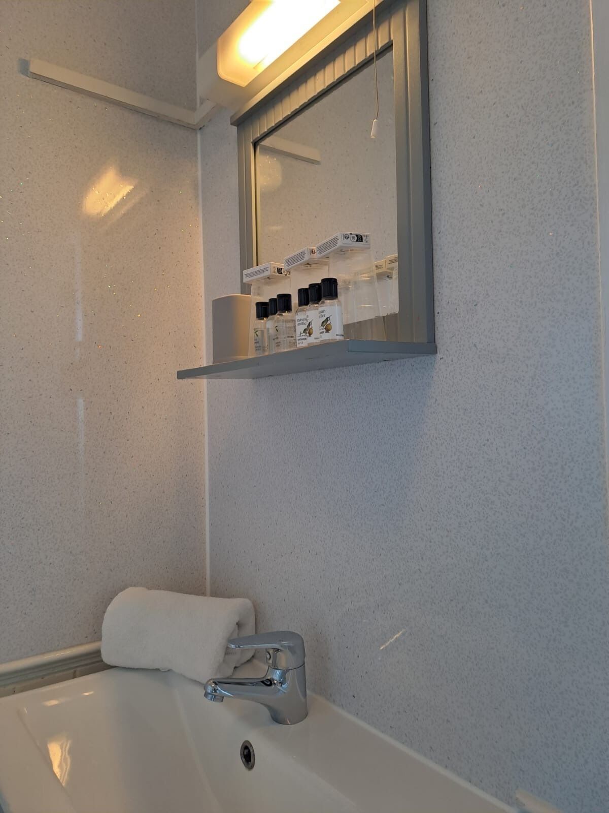 A bathroom with a white bathtub, a towel, a mirror, and a shelf with toiletries.