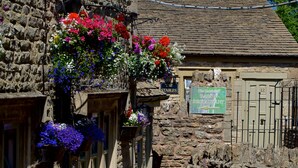 A stone building with hanging flower baskets, a sign for 'The Stable Inn & Restaurant', and a brick pathway leading to outdoor seating. - The Lamb Inn Great Rissington (Cheltenham)