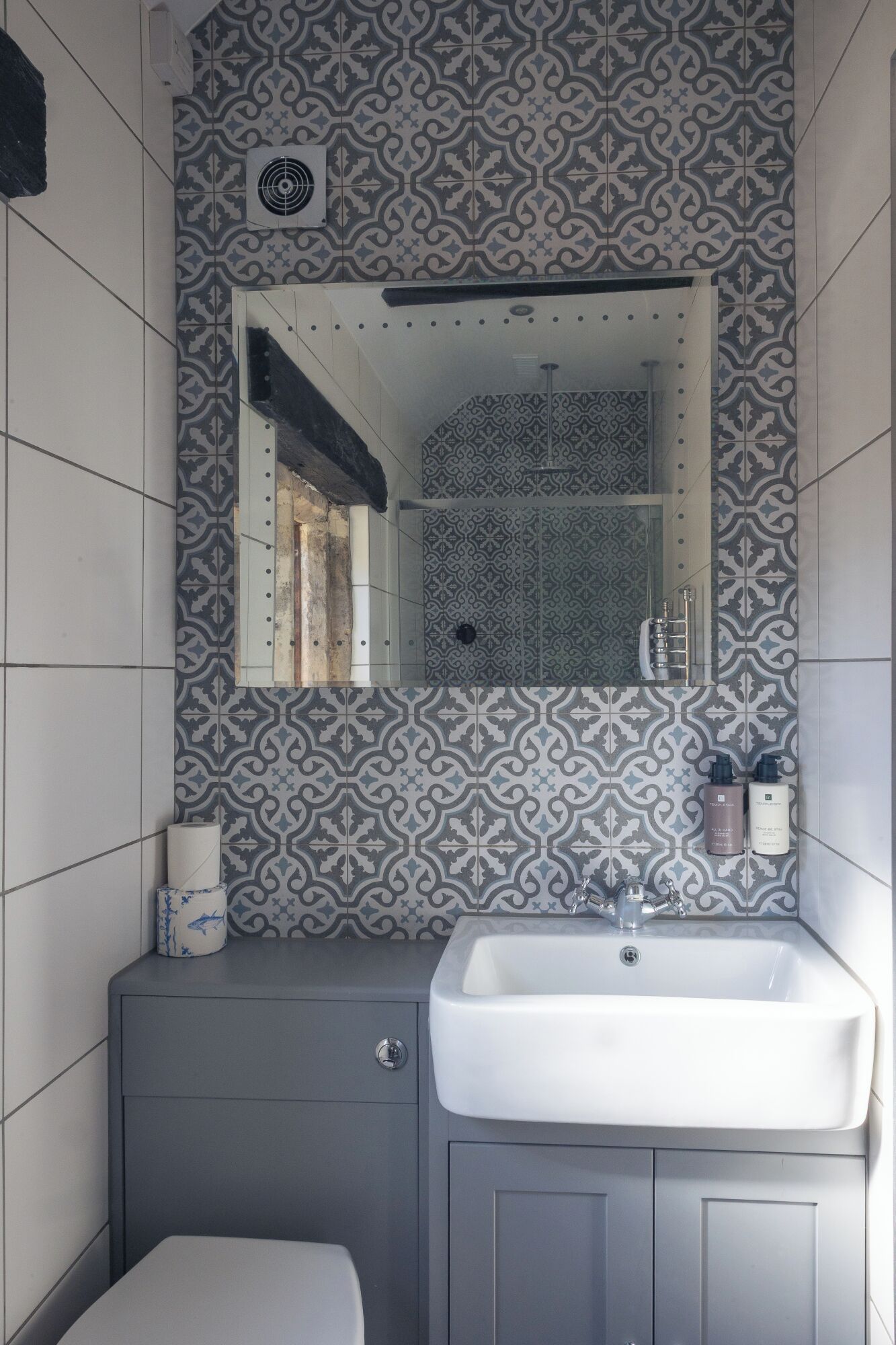 A bathroom with patterned tiles, a sink, a mirror, and a toilet.