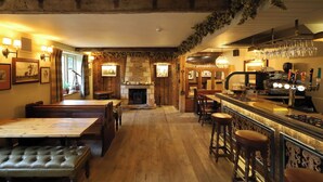A cozy bar area with wooden flooring, bar stools, and a fireplace. - The Lamb Inn Great Rissington (Cheltenham)