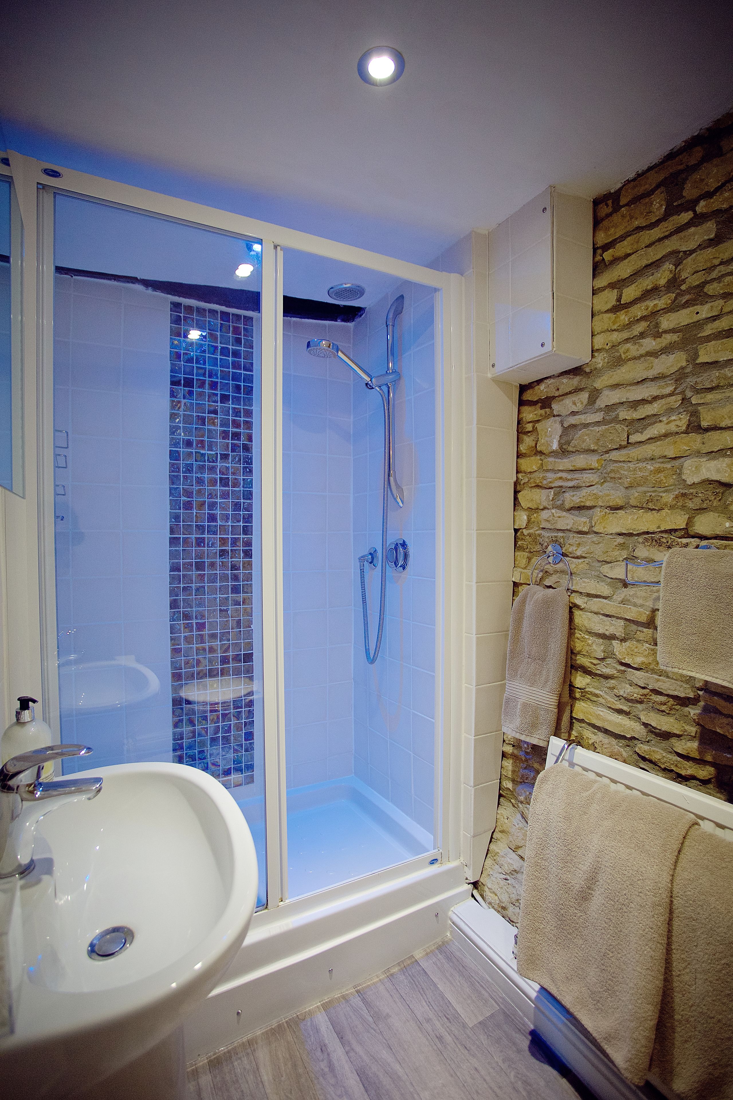 A bathroom with a glass-enclosed shower, a sink, and a stone wall.