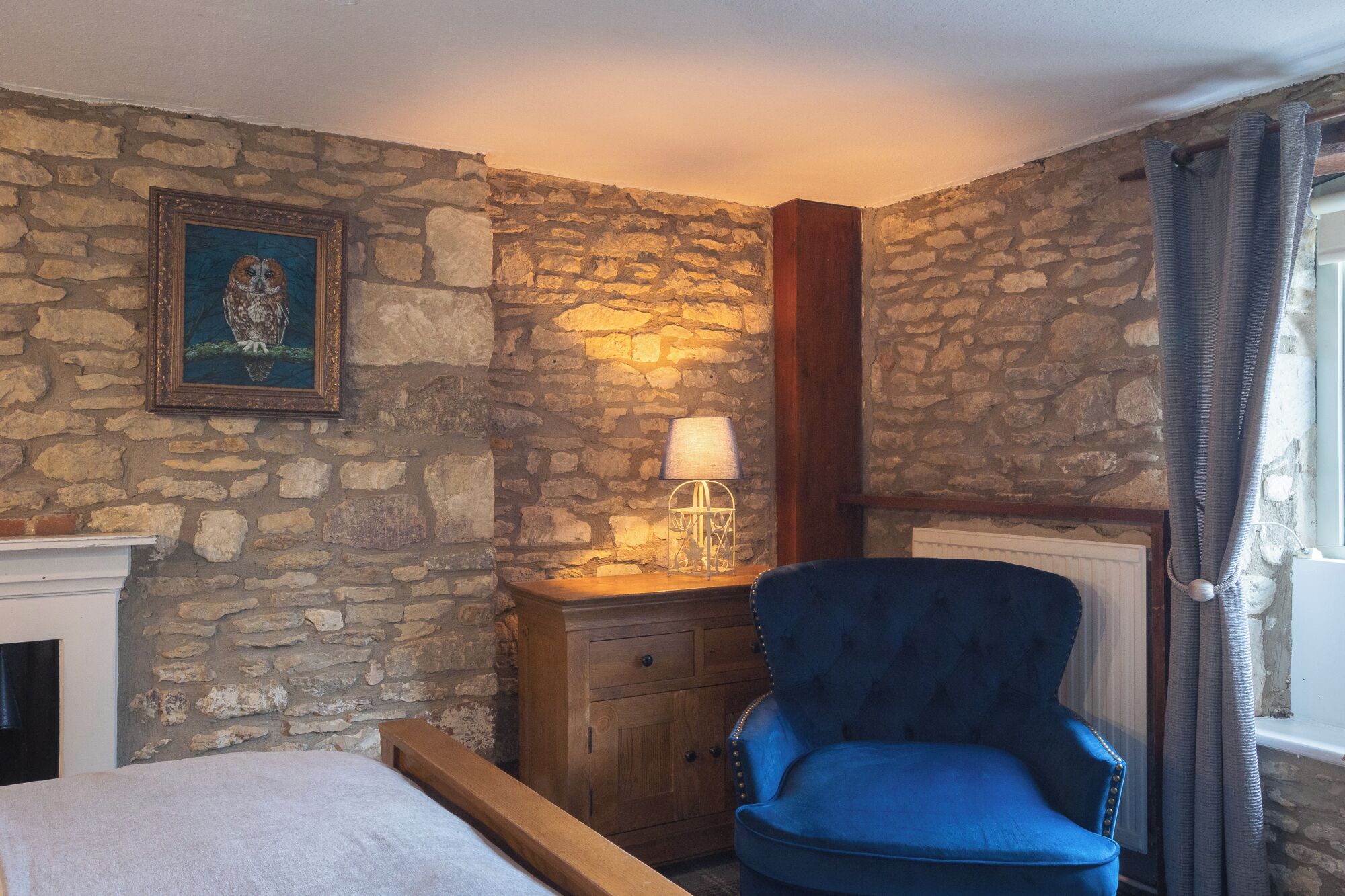 Ein Schlafzimmer mit Steinwänden, einem Holzkabinett, einem blauen Sessel und einem gerahmten Bild an der Wand.