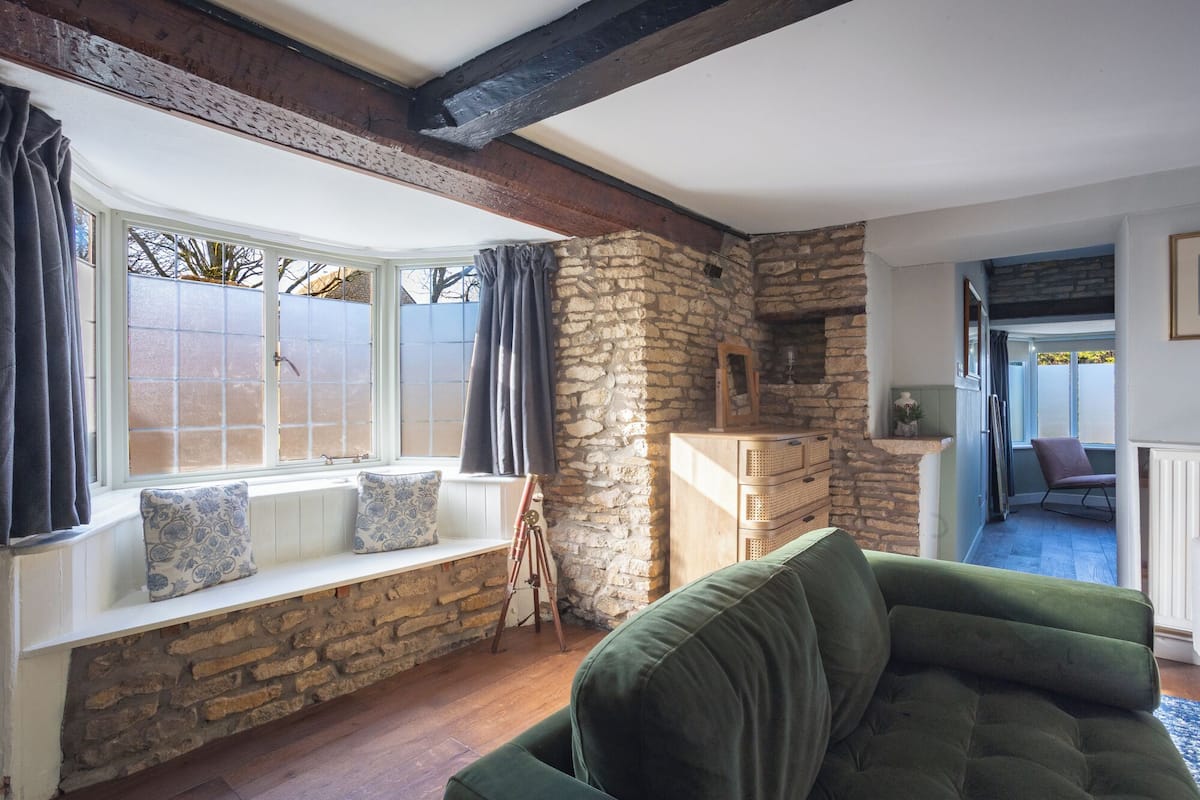 A cozy room with a stone wall, a bench with cushions, a green sofa, and a wooden cabinet.