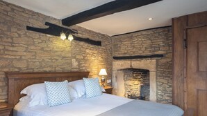 A bedroom with a stone wall, a wooden bed frame, and a stone fireplace. - The Lamb Inn Great Rissington (Cheltenham)