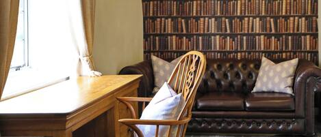 Un salón acogedor con un escritorio de madera, un sofá de cuero y una estantería llena de libros.