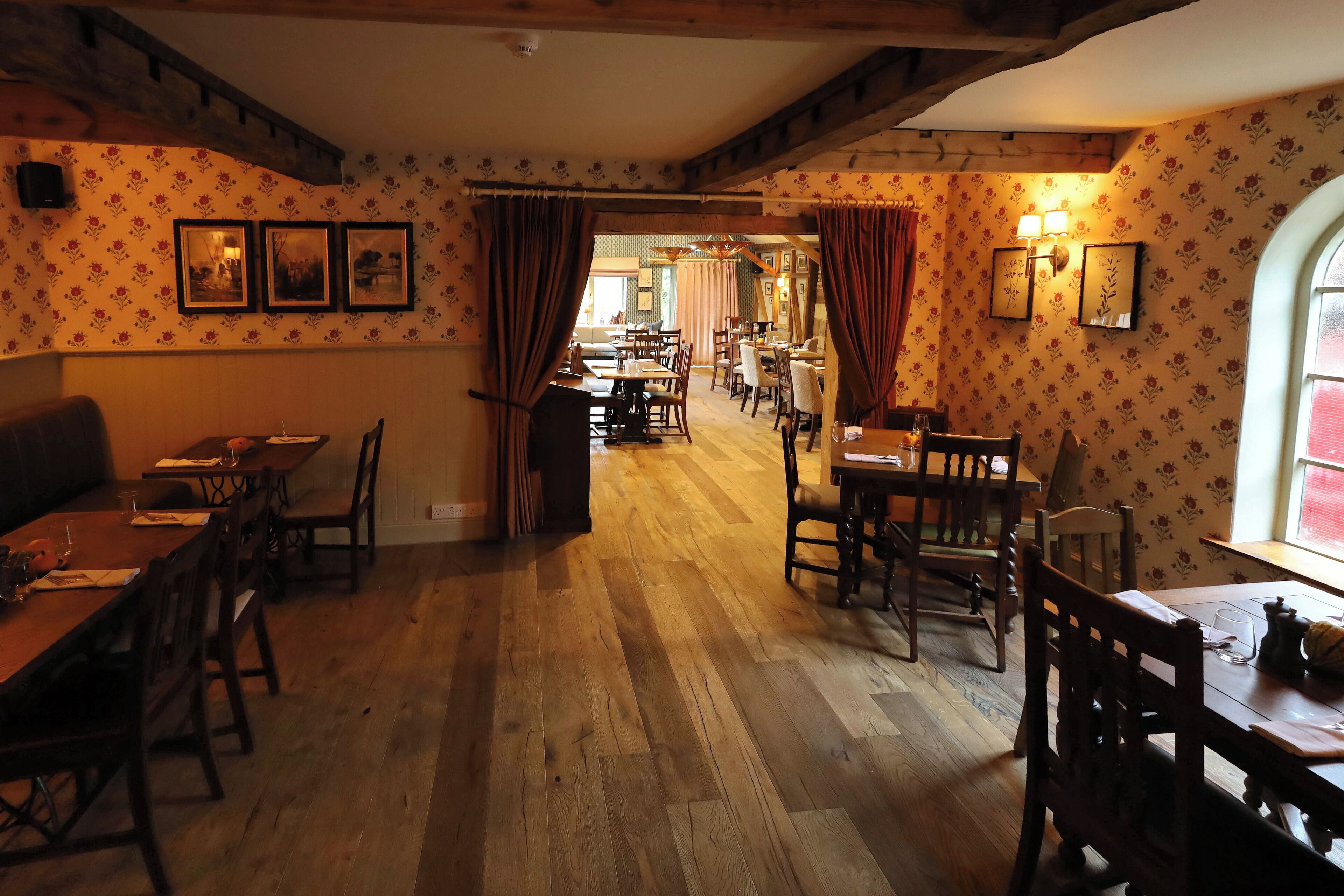 A dining area with wooden tables and chairs, a wooden floor, and floral wallpaper.