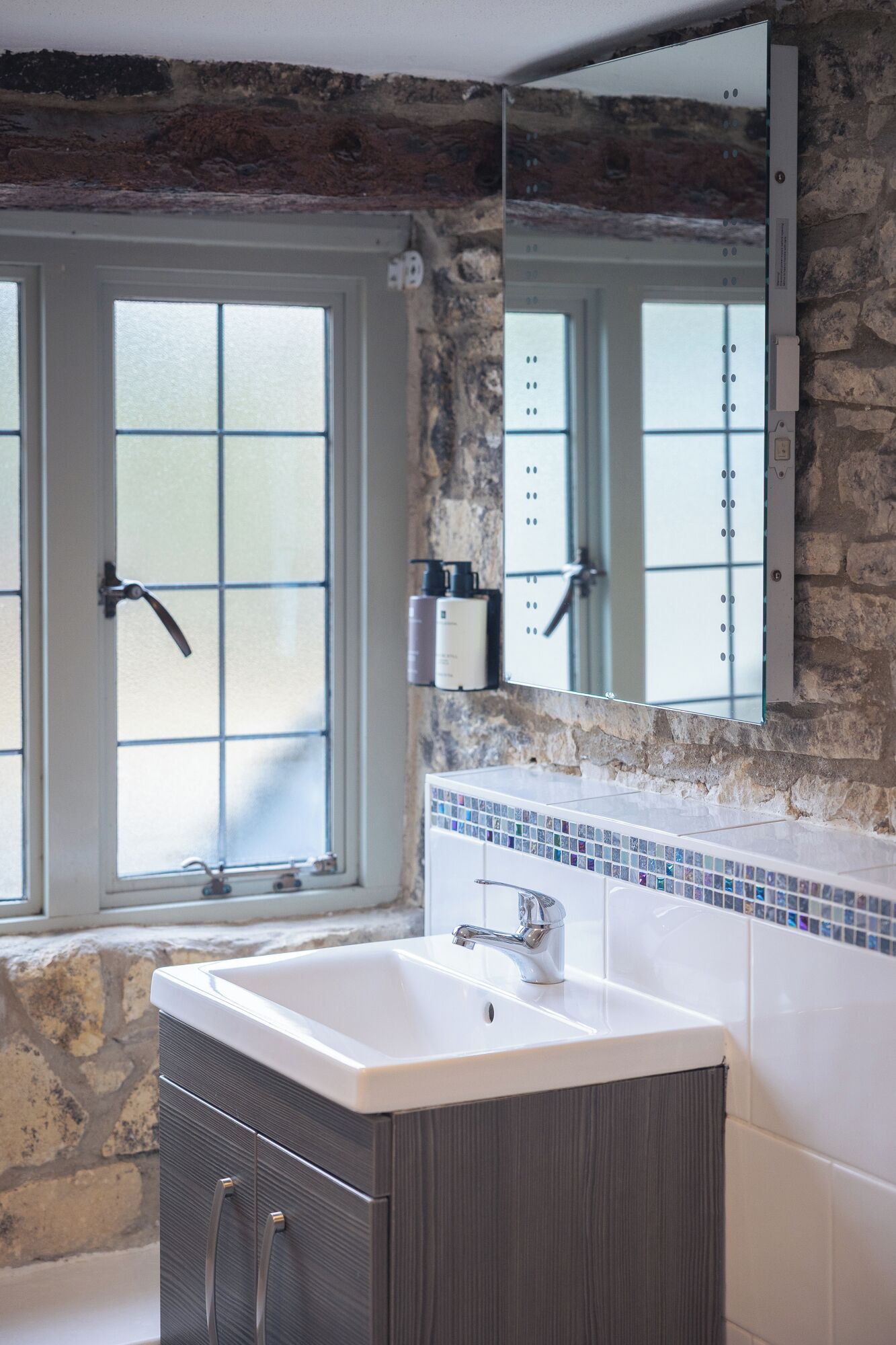 A bathroom with a large bathtub, a window with frosted glass, and a stone wall.