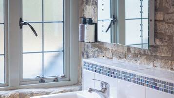 A bathroom with a large bathtub, a window with frosted glass, and a stone wall.