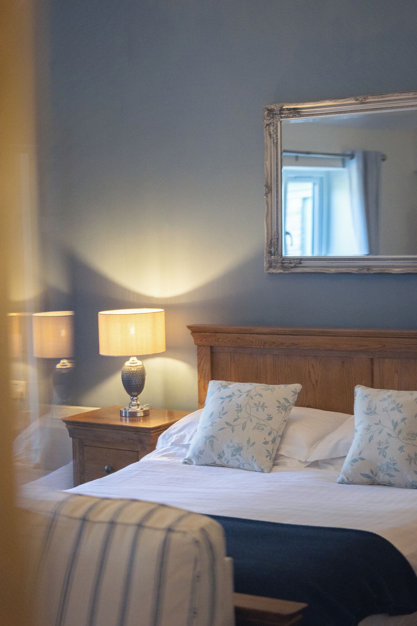 A hotel room with a bed, two bedside lamps, a wooden headboard, and a mirror on the wall.