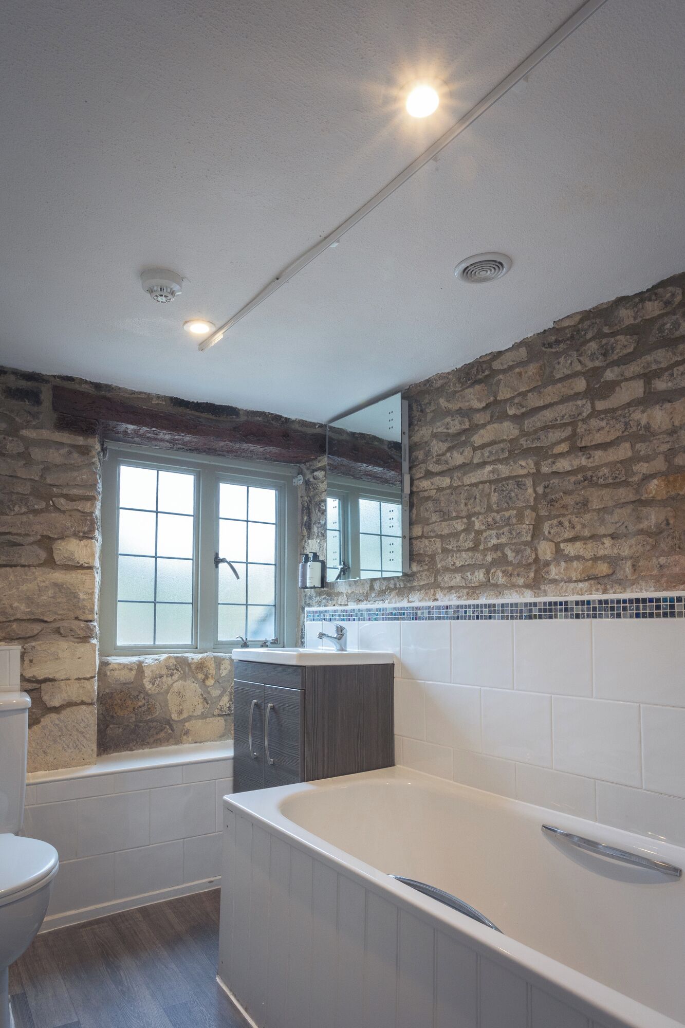 A bathroom with a stone wall, a window, a bathtub, a toilet, and a sink.