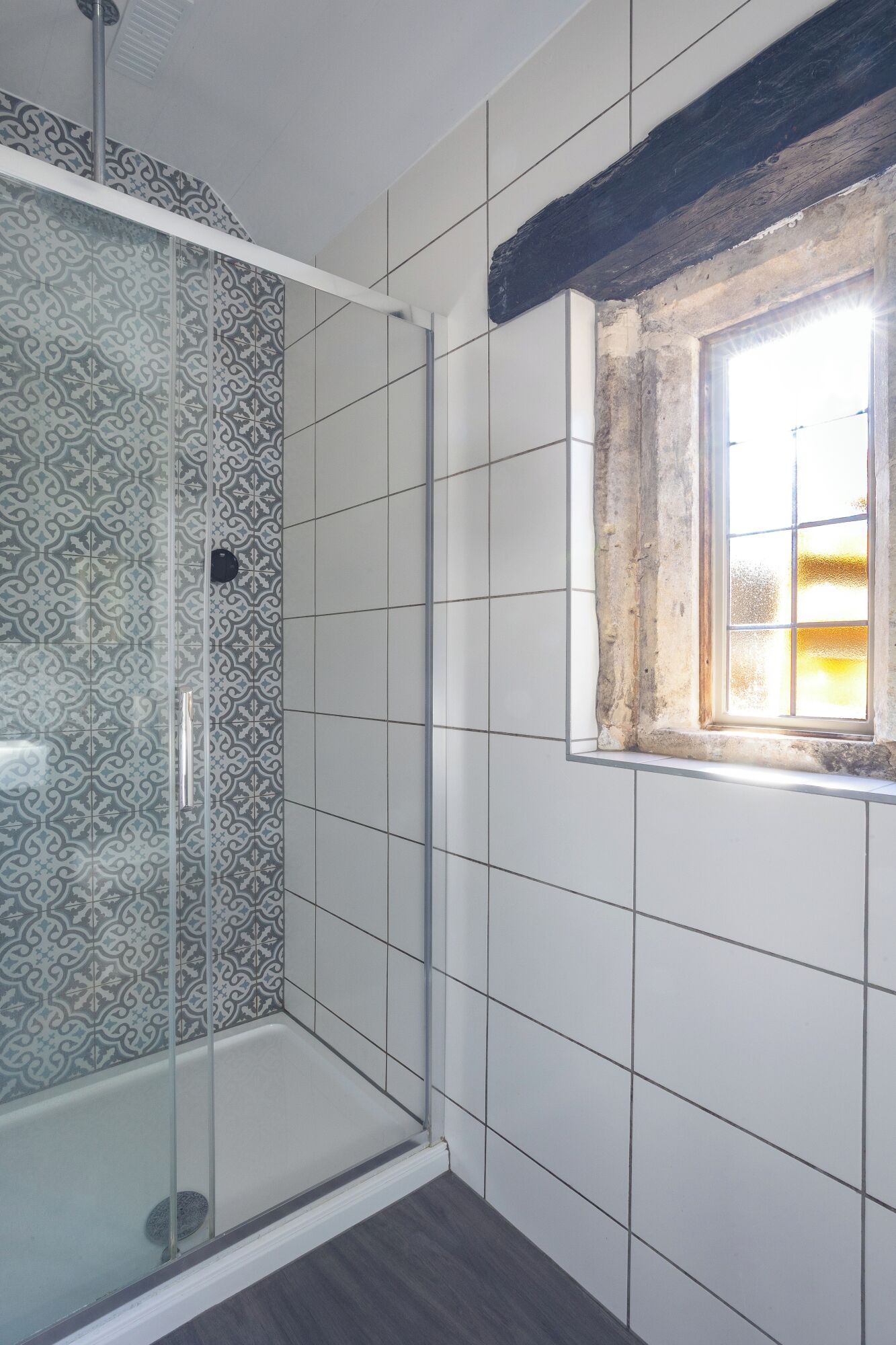 Chuveiro com azulejos estampados, porta de vidro e janela com vista.
