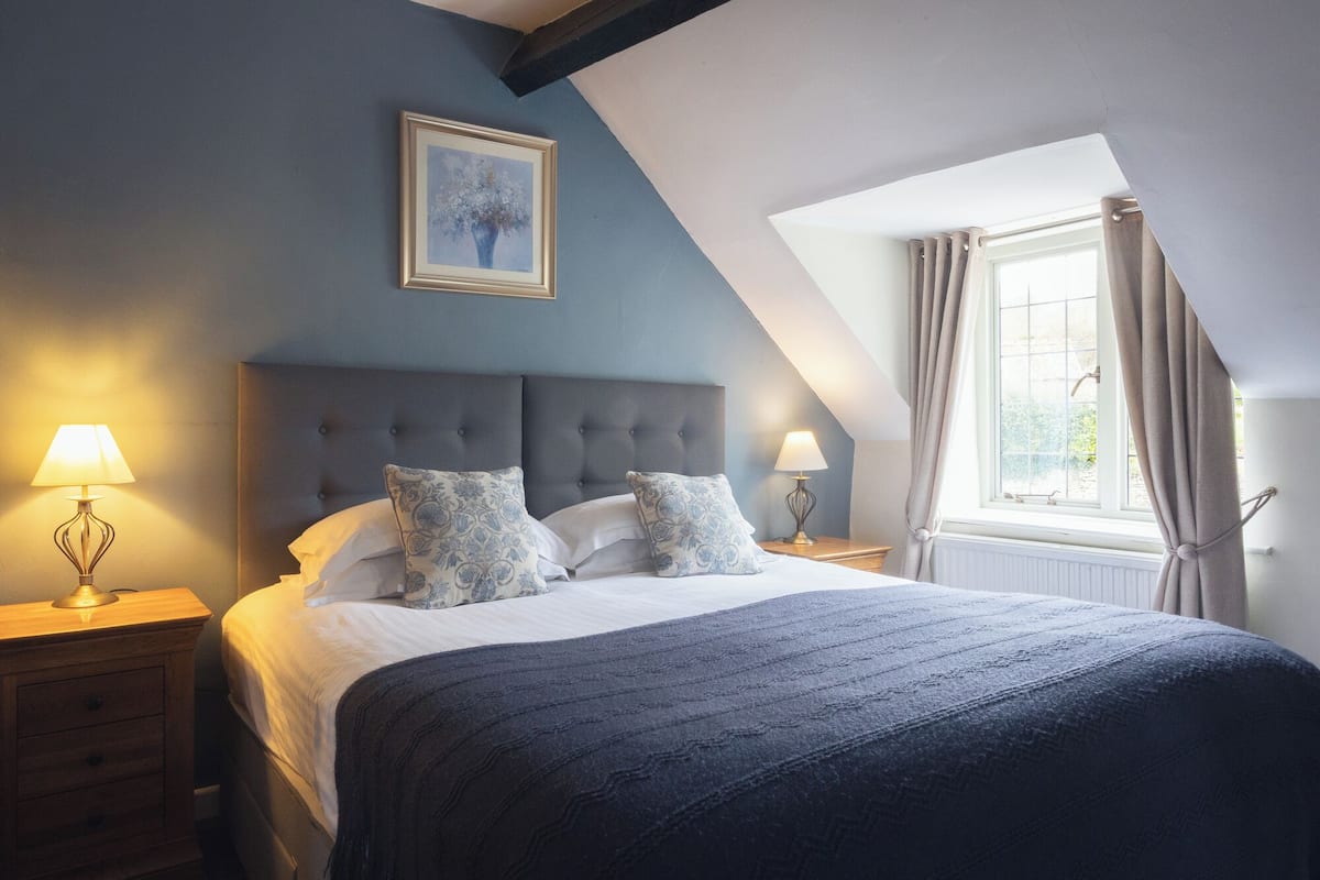 A bedroom with a large bed, two nightstands, a framed picture on the wall, and a window with curtains.