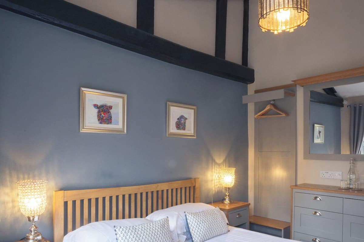 A bedroom with a wooden bed, bedside tables with lamps, a hanging light fixture, a dresser, and two framed pictures on the wall.