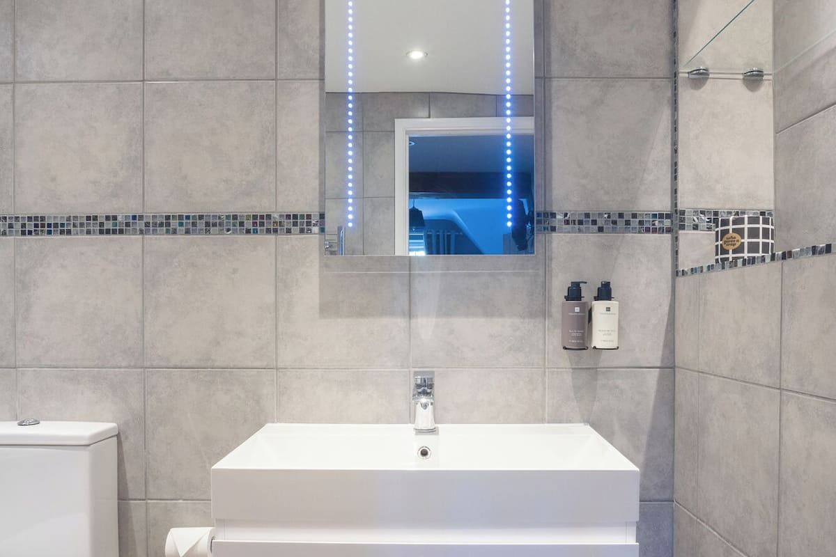 A modern bathroom with a white vanity, a large mirror with LED lights, and a tiled backsplash.