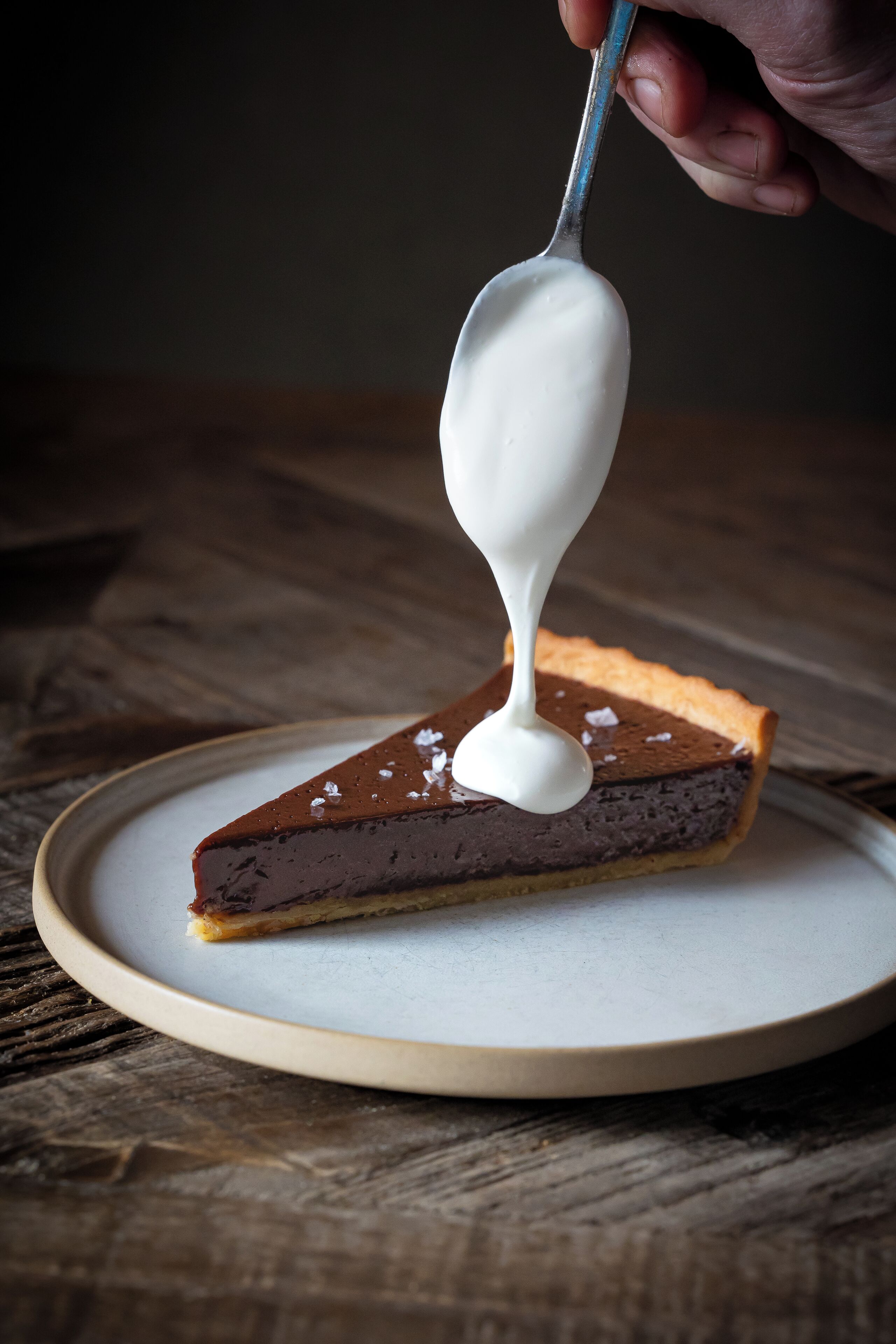 A slice of pie with a spoonful of white sauce being poured on top.