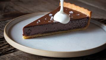 A slice of pie with a spoonful of white sauce being poured on top.