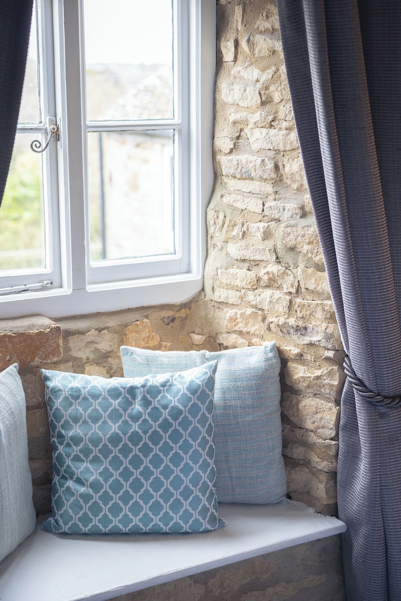A stone wall, a window with a white frame, and a cushion with a geometric pattern.