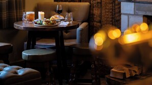 A cozy room with a wooden wall, a framed horse painting, a table with drinks and snacks, and a lit candle. - The Lamb Inn Great Rissington (Cheltenham)