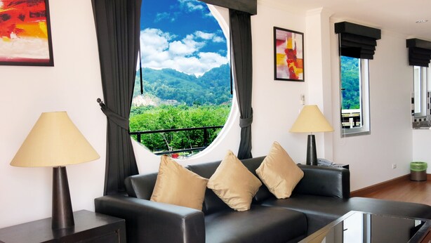 Una sala de estar moderna con un sofá de cuero negro, cojines color beige y dos lámparas de pie. Un ventanal ofrece vistas a un paisaje montañoso.