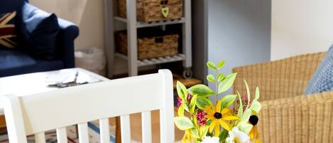 A cozy living area with a dining table, a vase of flowers, a sofa, and a kitchen area in the background.