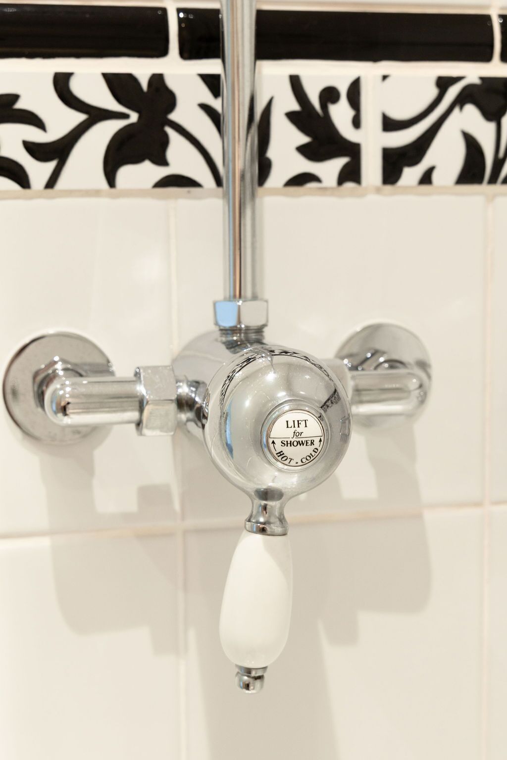 A bathroom with a shower control valve labeled "LIFT for SHOWER HOT - COLD" and a white handle.