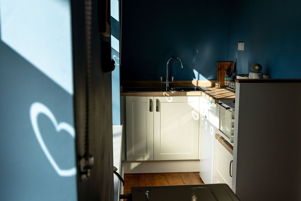Une cuisine étroite avec des meubles blancs, un robinet noir et un four à micro-ondes.