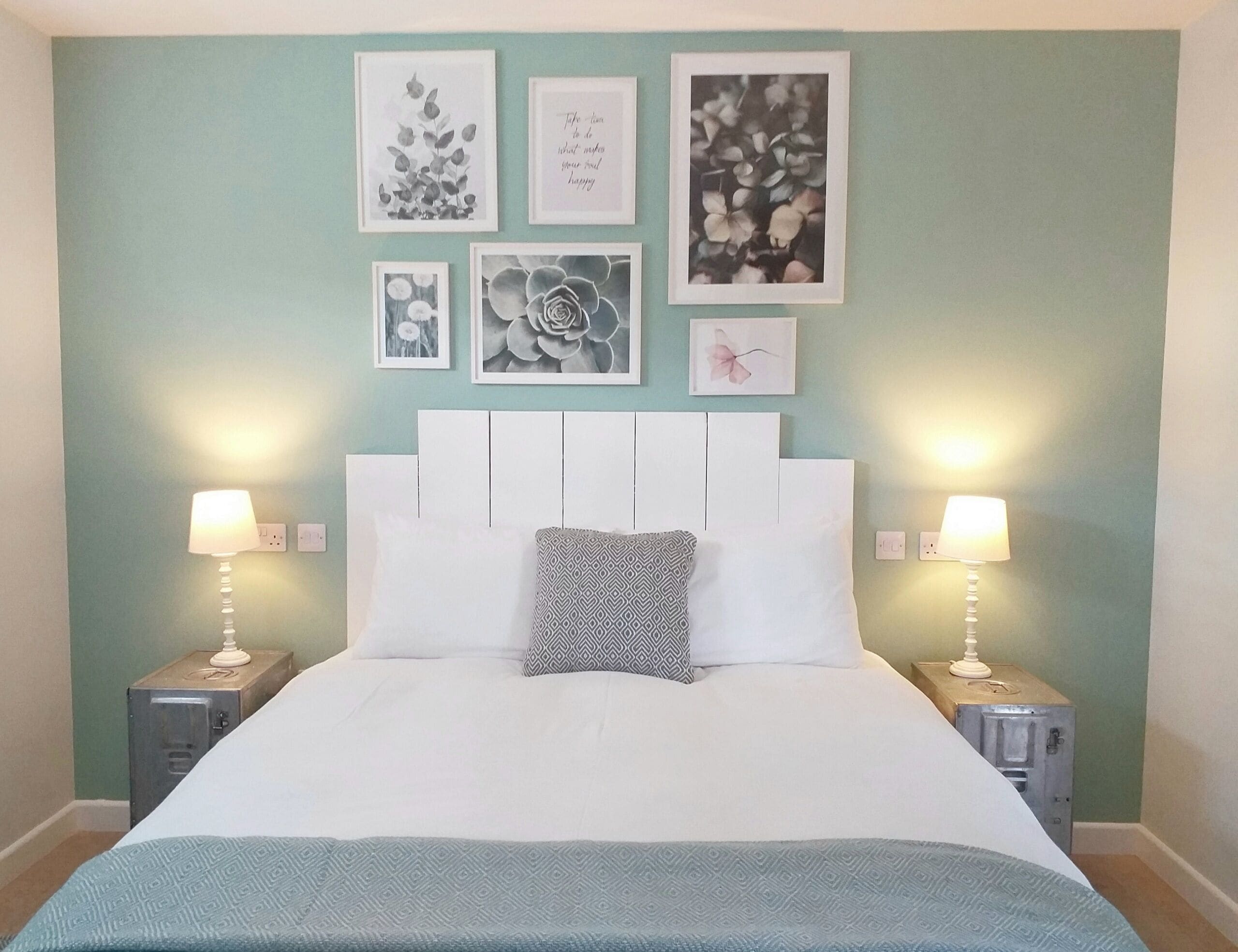 Un dormitorio con una cama, dos mesitas de noche y una pared decorada con marcos.
