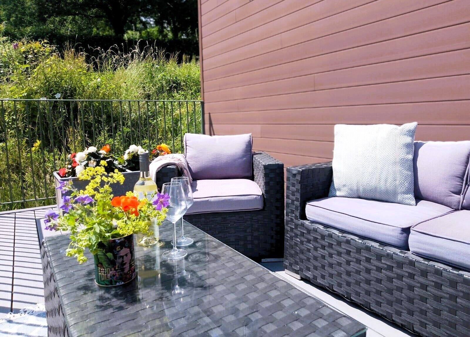 A patio with wicker furniture, a glass table, and a flower arrangement.