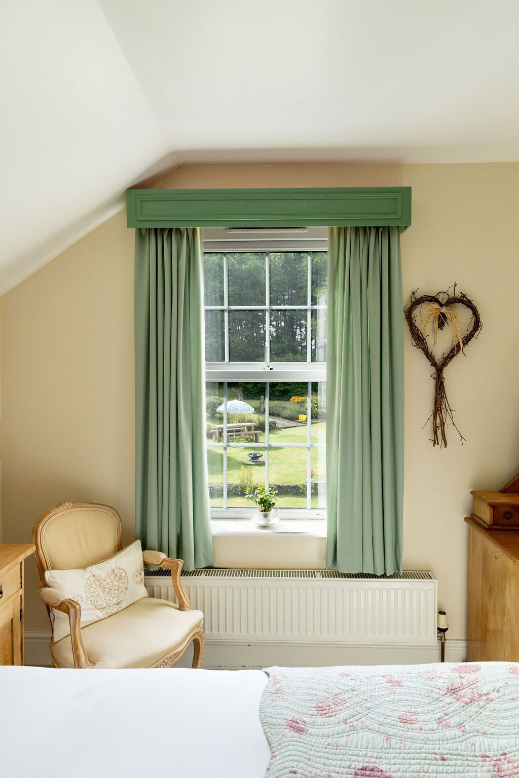 A bedroom with a large window, a heart-shaped decoration, and a view of a garden.