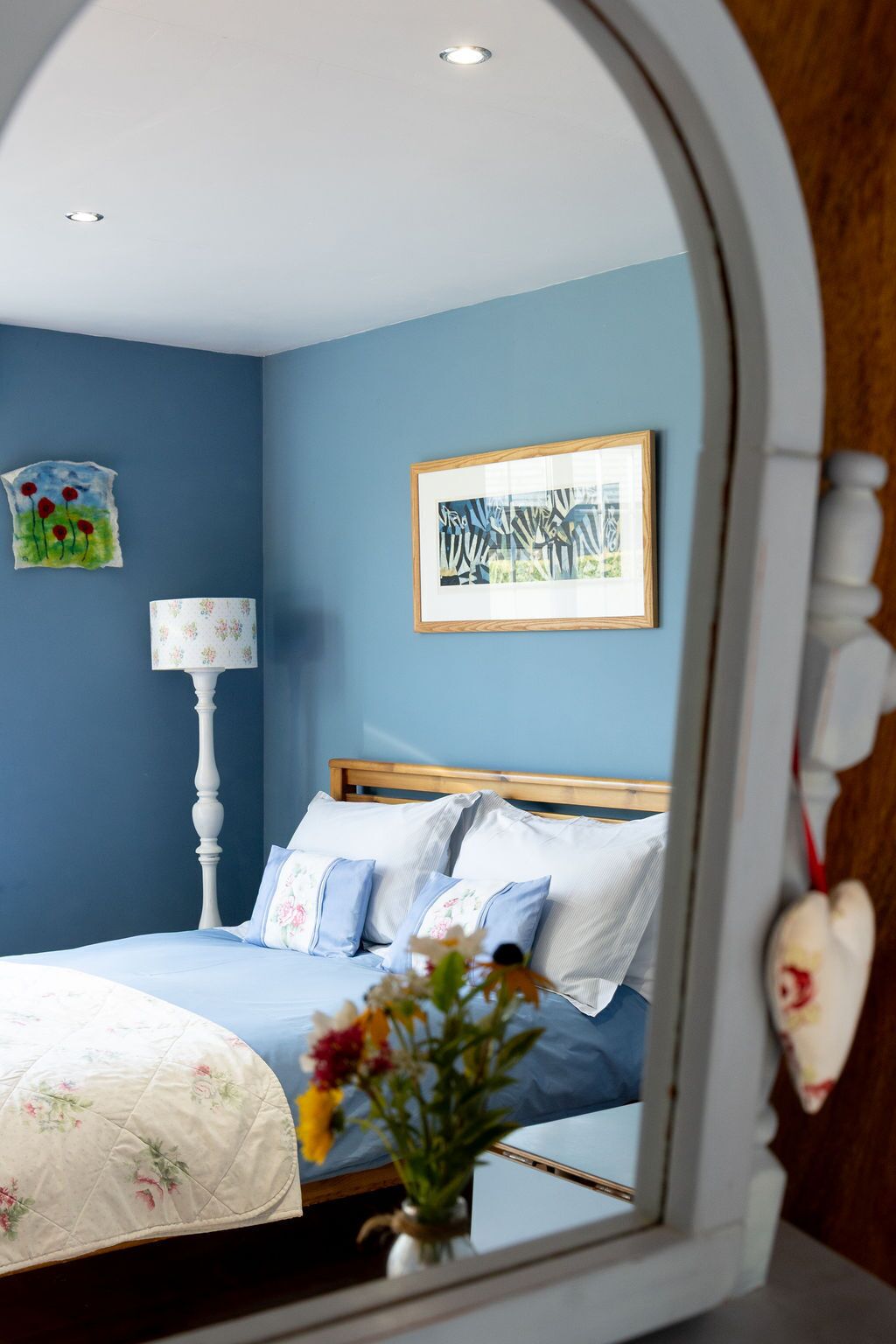 Une chambre à coucher avec un lit, un miroir, une lampe et un tableau encadré accroché au mur.