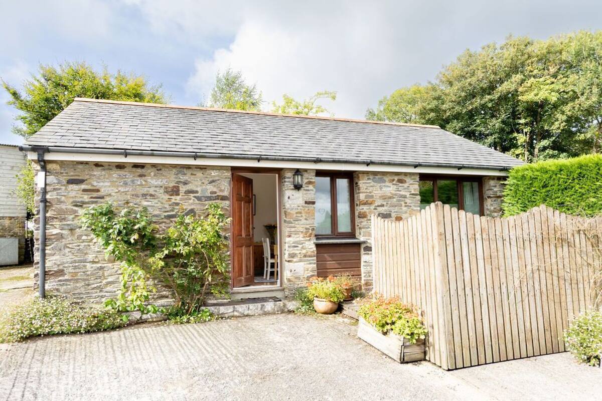A stone house with a wooden fence, a gravel driveway, and potted plants.