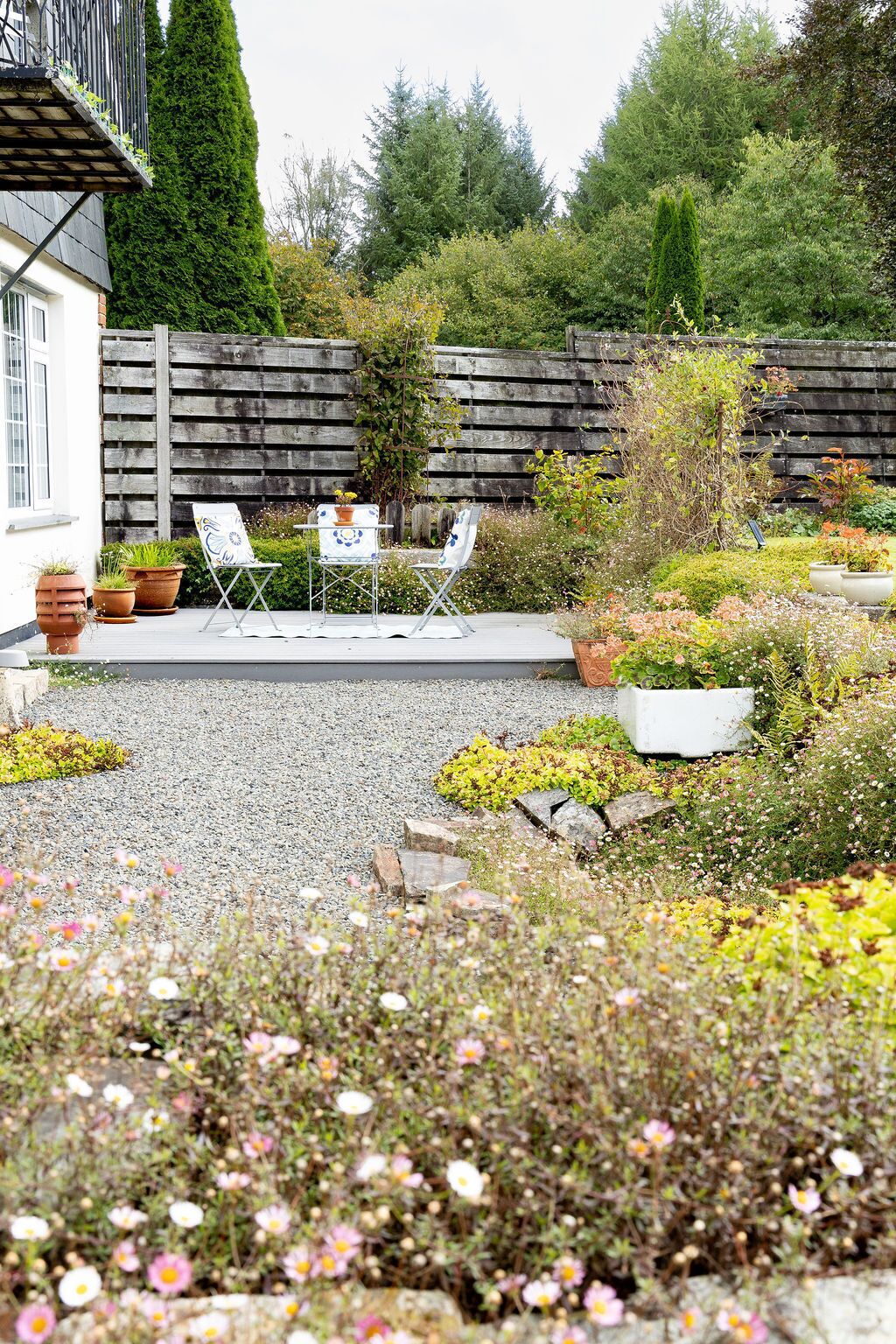 A garden patio with a table and chairs, surrounded by various plants and flowers.