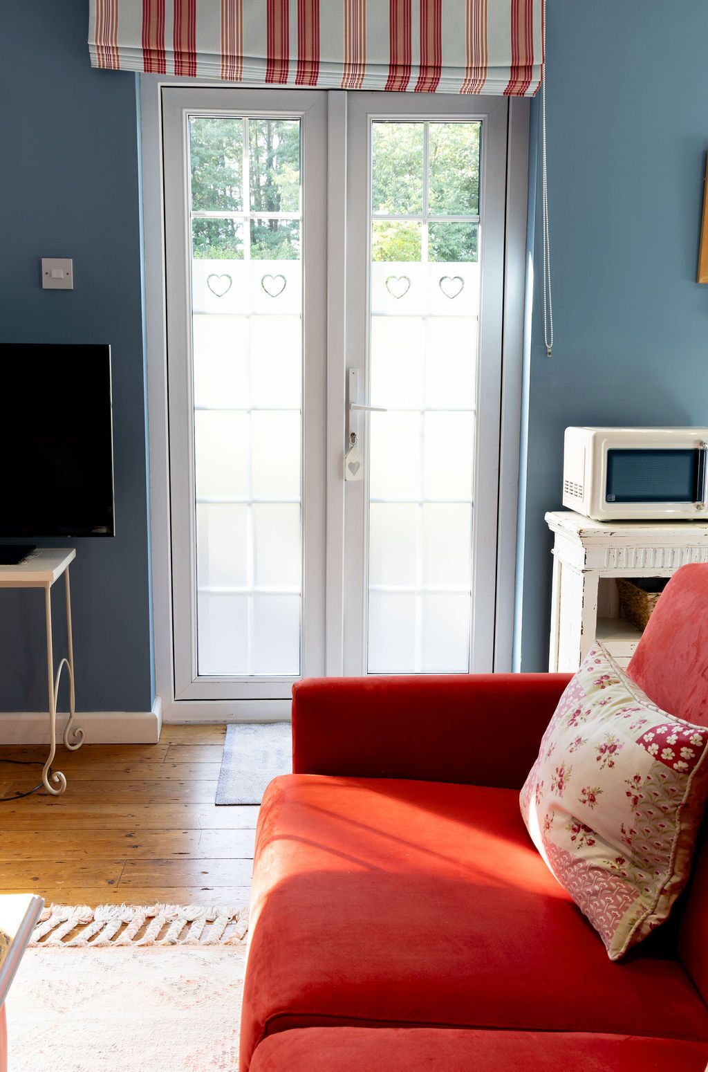 Un salon avec un canapé rouge, un téléviseur et un four à micro-ondes posés sur un meuble blanc.