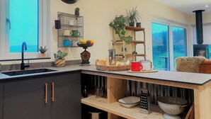 A modern kitchen with a built-in sink, a clock on the wall, and a view of the outdoors through large windows. - Lobhill Farmhouse (Okehampton)