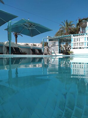 A clear blue pool with lounge chairs and umbrellas, surrounded by a white fence and palm trees. - Hotel Le Beau Sejour (Mezraia)