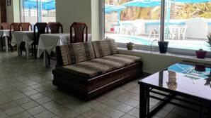 A dining area with tables and chairs, a sofa, and a view of a pool with umbrellas. - Hotel Le Beau Sejour (Mezraia)
