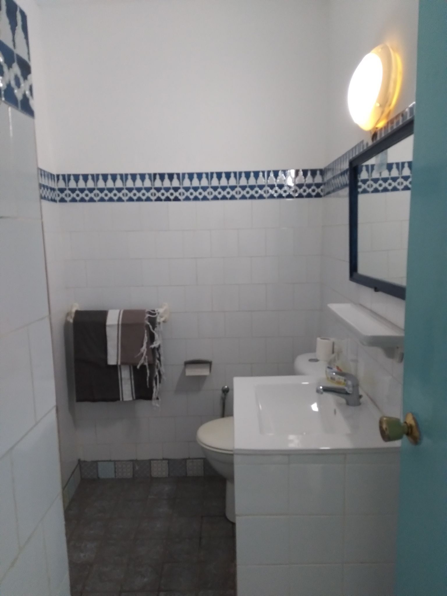 A bathroom with white tiles, a toilet, a sink, and a towel rack.