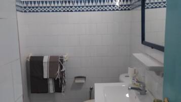 A bathroom with white tiles, a toilet, a sink, and a towel rack.