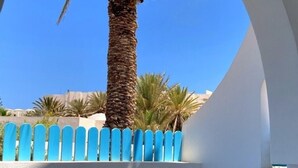 A room with a view of palm trees through an arched window, a tiled floor, and a white wall with a black tile accent. - Hotel Le Beau Sejour (Mezraia)