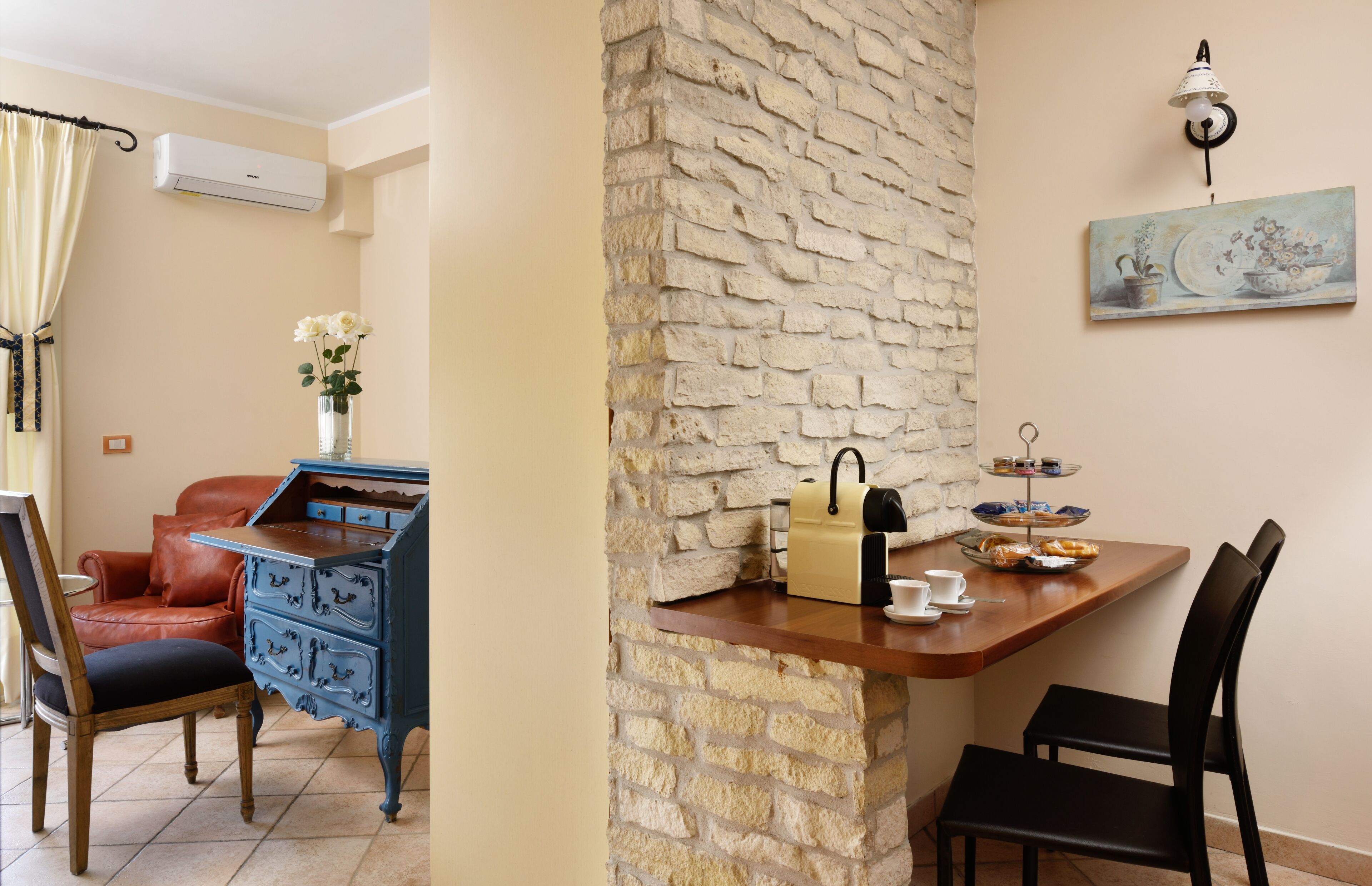 Una habitación con pared de piedra, una mesa de madera con un juego de té, un armario azul, una silla roja y un cuadro en la pared.