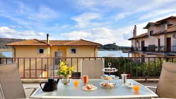A balcony with a table set for breakfast, overlooking a lake and buildings.