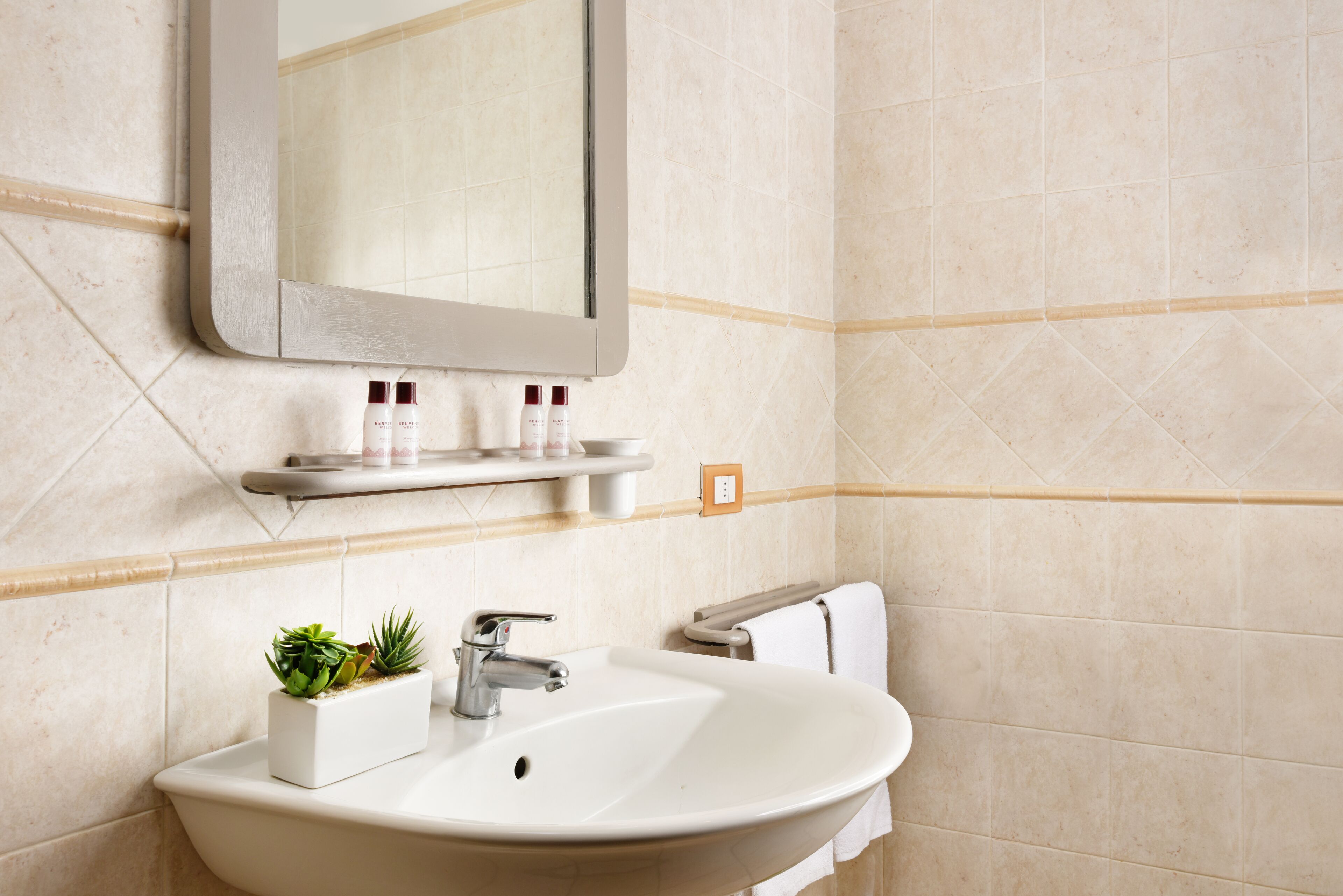 Une salle de bain avec un lavabo blanc, un miroir et une étagère contenant des articles de toilette.