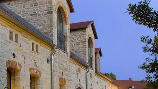 An outdoor dining setup with a table set for a meal, surrounded by stone buildings and outdoor seating. - Hotel Burg Wanzleben (Wanzleben-Börde)