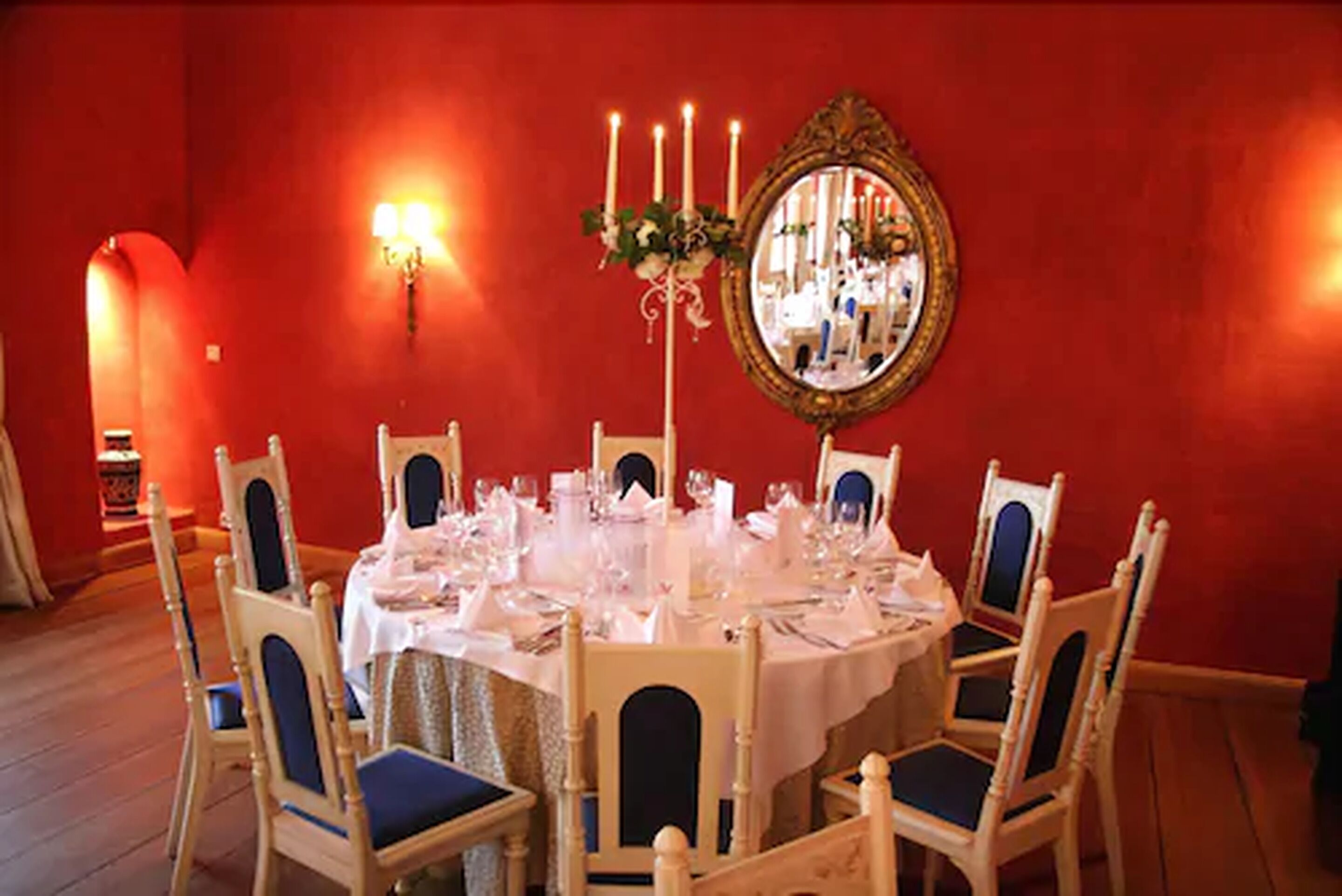 A dining room with a round table set for six, surrounded by six chairs with blue cushions.