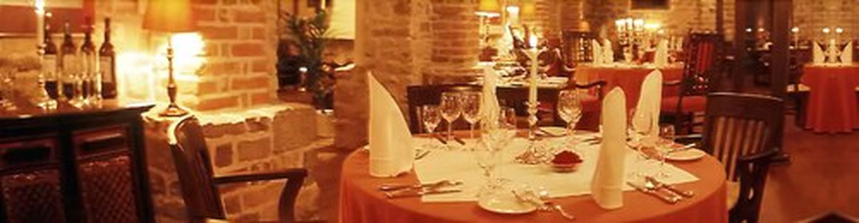 Un comedor iluminado con luz cálida, con una pared de ladrillo, una mesa redonda dispuesta para una comida y velas sobre la mesa.