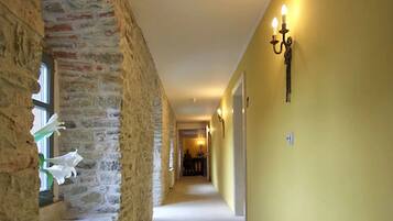 A hallway with stone walls, a carpeted floor, and a yellow wall with a wall sconce.