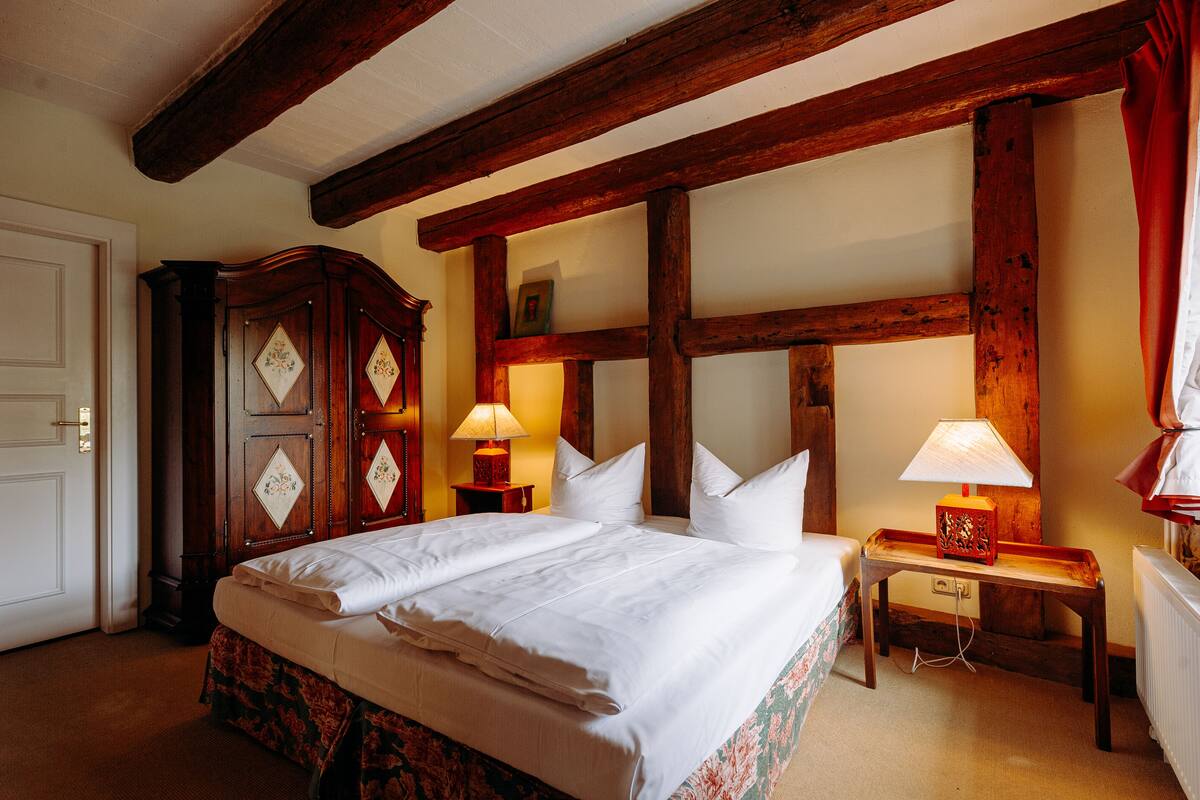Una habitación de hotel con una cama grande, vigas de madera, un aparador y dos lámparas de noche.
